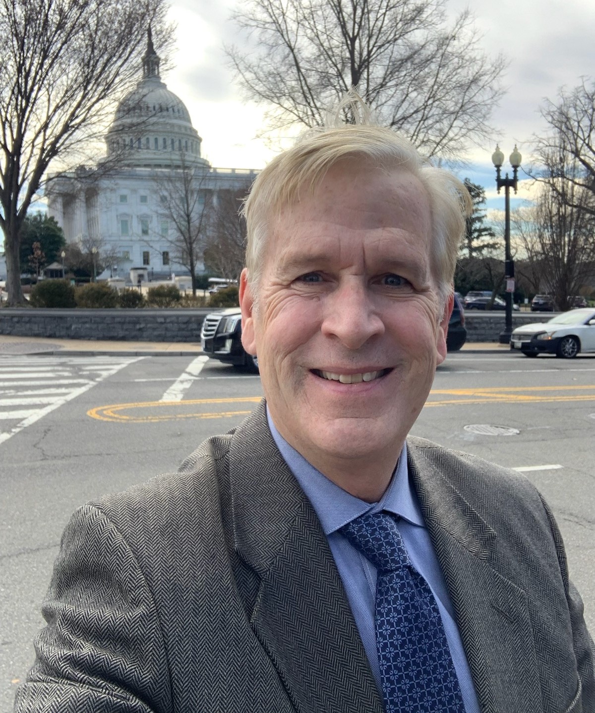 A portrait of Michael Brogioli with the U.S. Capitol building and some leafless winter trees in the background.